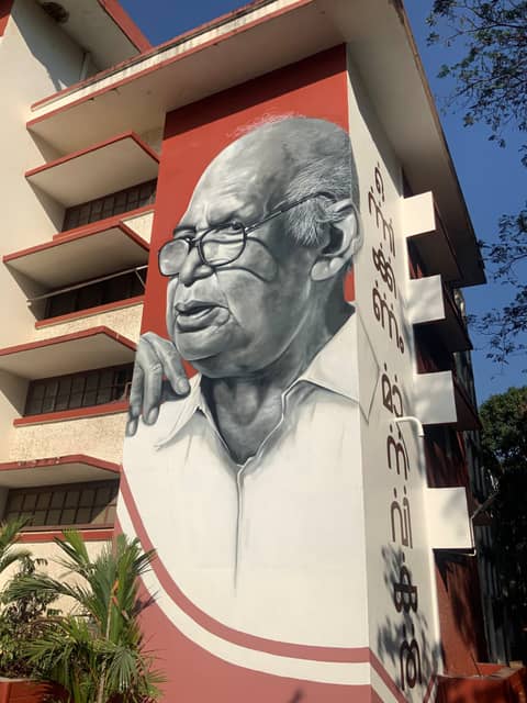 Elder with glasses, red building facade, Thrissur